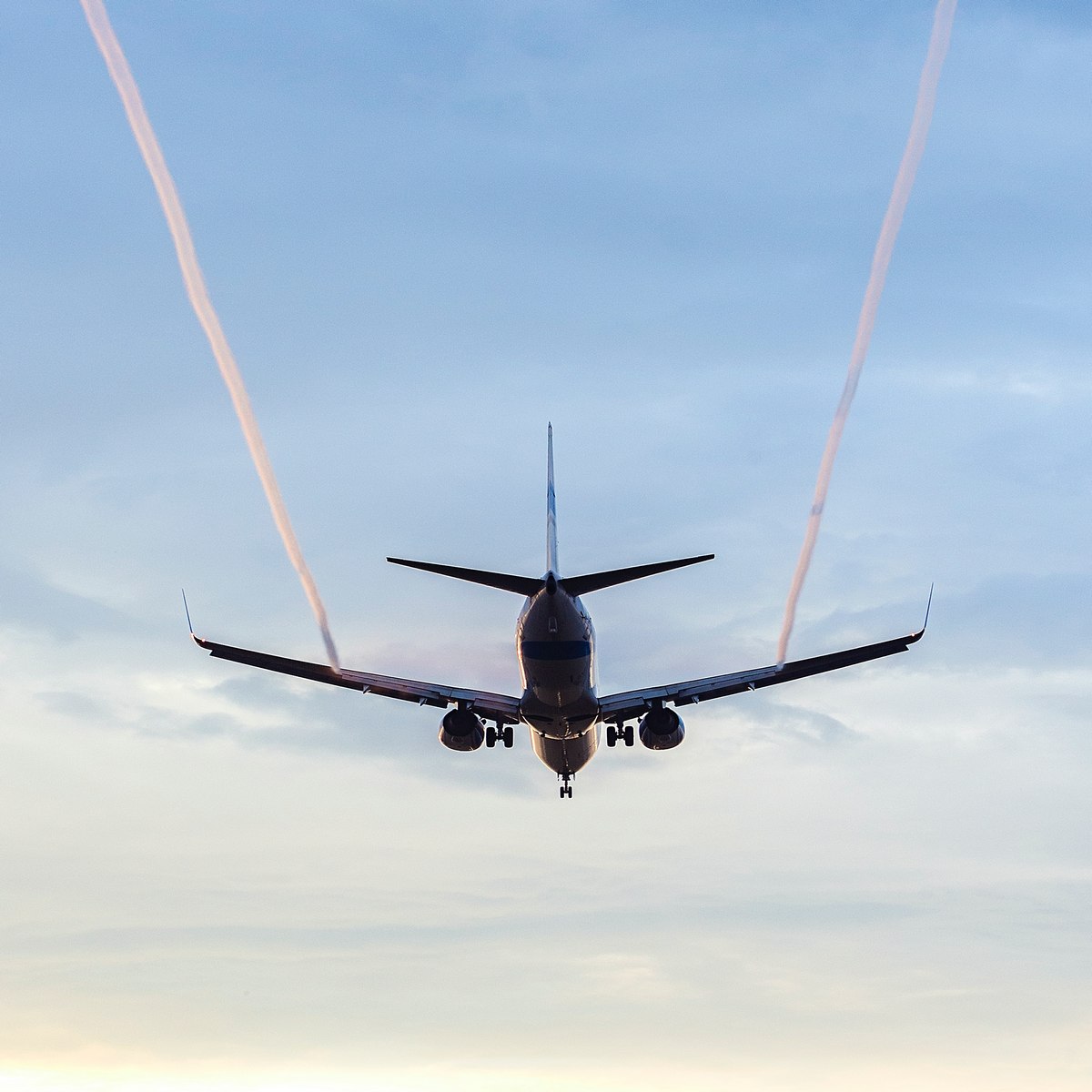 letadlo v letu z pohledu zezadu, s růžovými kondenzačními stopami na obloze