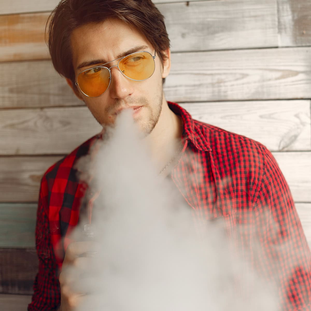muž v červené kostkované košili s oranžovými slunečními brýlemi, vydechující oblak kouře
